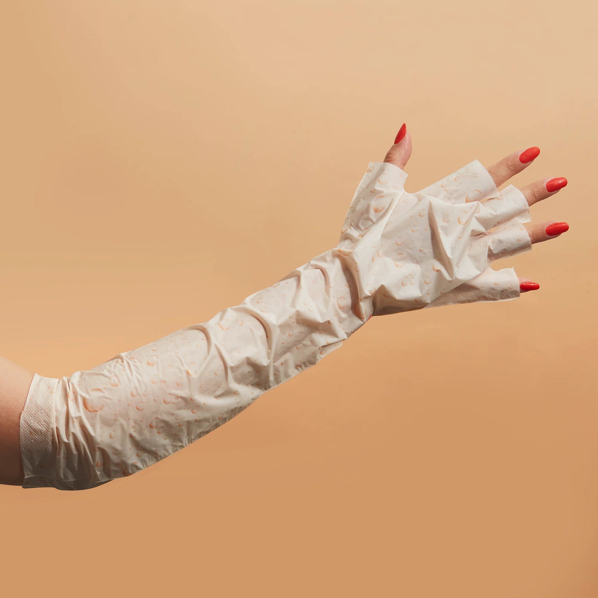 White disposable gloves worn by a person with red nail polish on a beige background